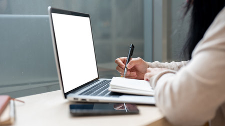 A close-up side view image of an Asian woman working remotely from a coffee shop, using a laptop...