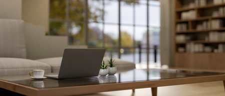 A close-up image of a laptop computer, a coffee cup, and decor plants on a coffee table in a contemporary living room. home workspace concept. 3d render, 3d illustrationの写真素材