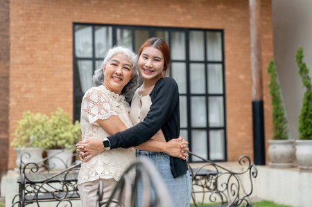 A happy, kind, mature Asian grandma is hugging her lovely granddaughter in a home garden on a bright day, spending time together at home. embrace with love, grandparent home visit, family bondingの写真素材