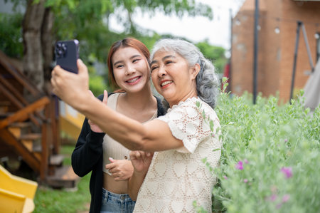 A lovely Asian grandma is taking a selfie or recording a video with her granddaughter while chilling together in a garden, having a happy time at home. family bonding, people and wireless technologyの写真素材