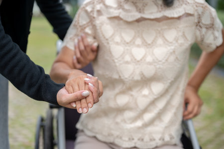 A close-up image of a caring granddaughter holding her grandma's hand, helping her stand up from the wheelchair and walk in a park. health care, caregiver and patient, family bondingの写真素材