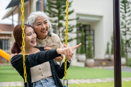 A happy Asian granddaughter is on a swing, enjoying a conversation with her grandma in their home backyard. happy moment, family bonding, togethernessの写真素材