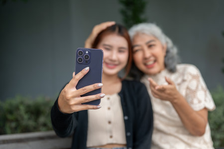 A selective focus image, a lovely Asian granddaughter and her grandma are sitting on a bench in a...