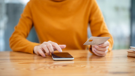A close-up image of a woman holding a credit card and using her smartphone, using a mobile banking app to pay bills online. cashless, online shopping, online payment, transferring moneyの写真素材