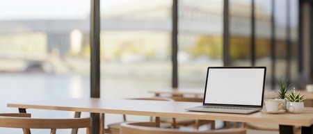 A laptop computer with a white-screen mockup on a wooden table by the window in a modern coffee shop co-working space. 3d render, 3d illustrationの写真素材