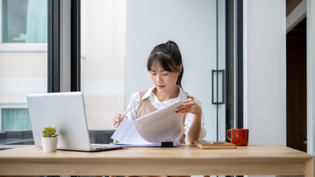 A beautiful, focused Asian businesswoman is reviewing business report at her desk, working in her private office. businesspeople conceptの写真素材