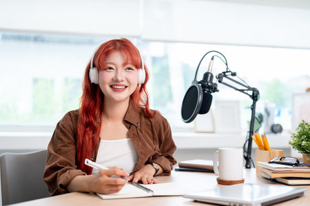 A charming Asian female podcaster or online radio host is listening to her guest's answers during a remote interview while conducting her podcast in the studio.の写真素材