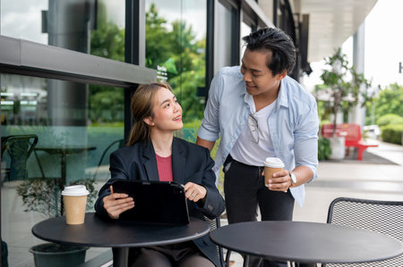 Two positive Asian colleagues or couple, a female and a male, are having an informal meeting at a coffee shop, smiling at each other.の写真素材