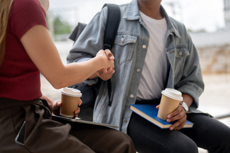 A cropped image of a female college student is shaking hands with her male friend while relaxing together in an outdoor hallway on campus. friendship and education conceptsの写真素材