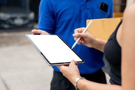 A close-up image of a female customer signing on a digital tablet before receiving her package from a delivery man in front of her house. a digital tablet with a white screen mockupの写真素材