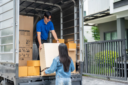 An Asian delivery man or mover in a blue uniform is unloading a cardboard box from his truck with...