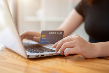 A close-up image of a woman holding a credit card while typing on a laptop keyboard at a table...