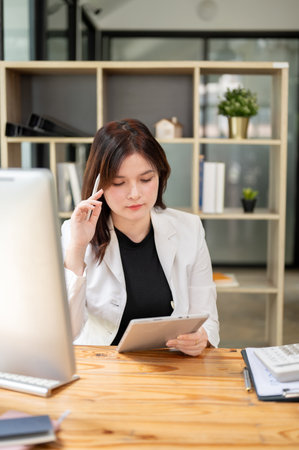 A thoughtful businesswoman in a formal suit using her digital tablet at her desk in the office, taking notes, thinking or planning a project. businesspeople and wireless technology conceptsの写真素材