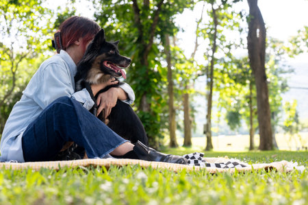 A caring and happy Asian woman is hugging her dog while sitting on a picnic cloth in a green park on a bright day, enjoying outdoor activities together. emotional support animal, pet, best friendsの写真素材