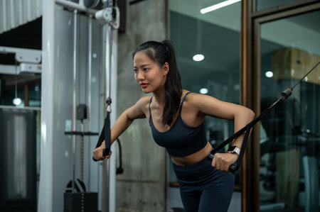 A sporty, fit Asian woman in athletic wear is working out on a multi-station machine at the gym, focusing on training her shoulders and arms. people and sport conceptsの写真素材
