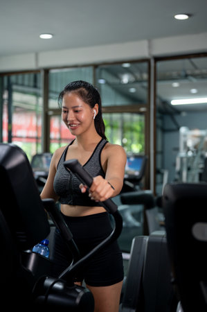 A beautiful, sporty Asian woman in sportswear, wearing earphones is focused on running on an...
