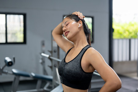 A beautiful, sporty Asian woman in athletic wear is stretching her neck, warming up before her...