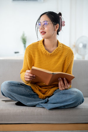 A beautiful, cheerful Asian woman in casual clothes is daydreaming while looking out the window and...