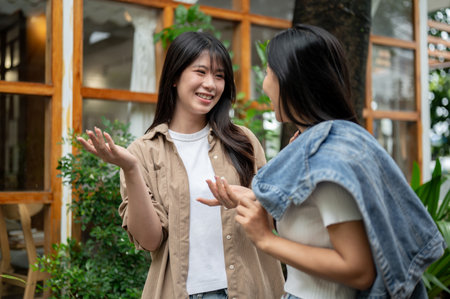 Two cheerful Asian female friends are enjoying a conversation while walking through a garden. gossiping, chatting, talkingの写真素材