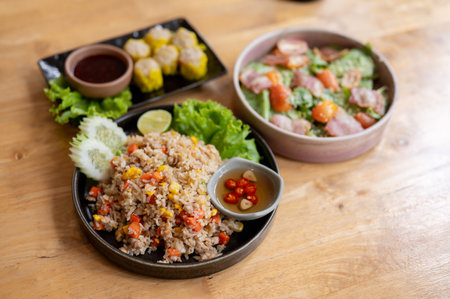 A wooden dining table at a restaurant or at home featuring a plate of fried rice, a salad bowl, and a plate of steamed dumpling. the concept of foodの写真素材