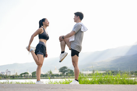 An active, sporty Asian couple in sportswear is stretching their legs and bodies, warming up before running together in the morning at a park with a stunning natural view.の写真素材
