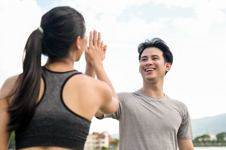 An active, happy Asian couple in sportswear gives each other a high five after running together in a...
