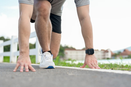A cropped image of an active man in sportswear in a ready-to-run position, preparing to sprint in a...