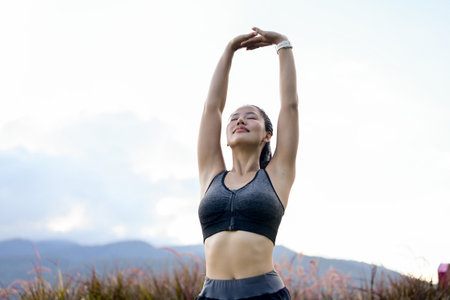 A beautiful, sporty Asian girl in sportswear is stretching her arms, warming up before her morning run and workout in the park. lifestyles, sport, outdoor activityの写真素材