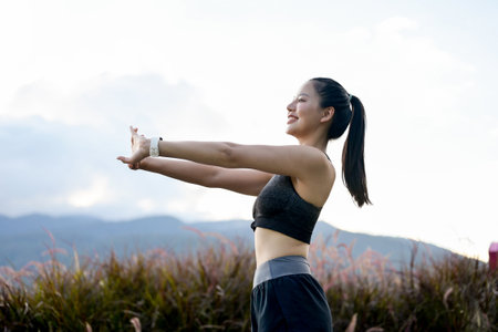 A beautiful, sporty Asian girl in sportswear is stretching her arms, warming up before her morning run and workout in the park. lifestyles, sport, outdoor activityの写真素材