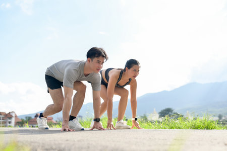 A confident, sporty Asian couple in sportswear is getting ready to sprint on a sunny day in the park. competition, marathon, runners, active lifestylesのeditorial素材