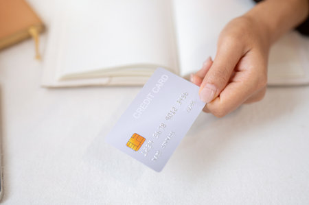 A top view of a woman's hand holding a credit card over a white table. financial, lifestyles, investment, credit card paymentの写真素材