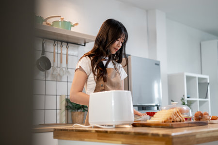 A charming young Asian woman is making toast with a toaster in her minimalist kitchen at home, preparing breakfast in the morning. living home, domestic life, food, and peopleの写真素材
