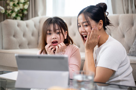 A young, adorable Asian girl and her mom are enjoying watching a scary movie through a digital tablet together in the living room, spending fun time at home.の写真素材
