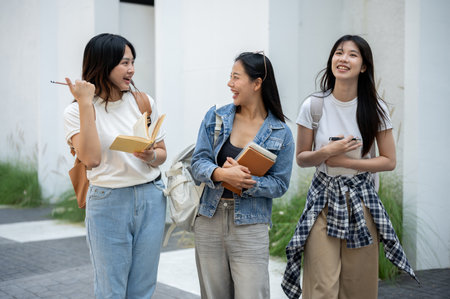 A group of cheerful Asian college students in casual clothes and backpacks enjoying a conversation while walking in their college. friendship, education, people, lifestylesの写真素材