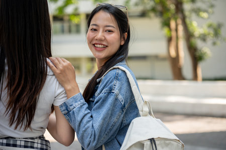 A beautiful, happy Asian female college student in casual clothes and a backpack is walking through her college campus on the way to class with her friends, turning back and smiling at the camera.の写真素材