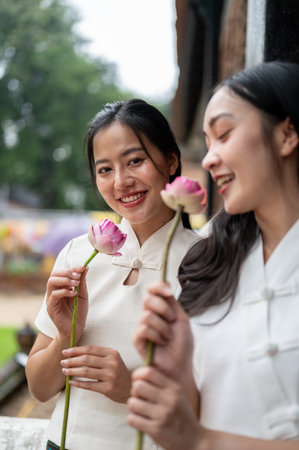 Two charming Asian women in traditional Northern Thai-Lanna dresses stand in a temple with beautiful lotuses in their hand. Thai culture, Buddhist, Asian travelingの写真素材