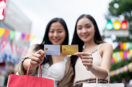 A close-up of two beautiful Asian women showing their credit card to the camera while standing in a city market, enjoying their shopping day together with cashless payments.の写真素材