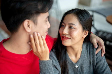 A sweet, lovely young Asian couple in cozy autumn clothes are having a romantic coffee date at a cafe. The girlfriend gently touches her boyfriend's face, expressing love and care.の写真素材