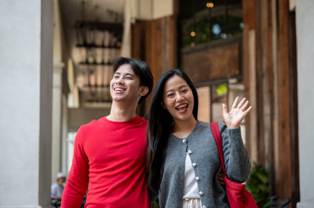 A portrait of a charming, lovely young Asian couple in cozy clothes, enjoying a weekend date as they stroll through the city and shop together, smiling and waving at the camera.の写真素材