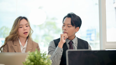 A professional, smart Asian male CEO or businessman sits attentively, focused on listening to his team's ideas during a business meeting in a modern office.の写真素材