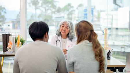 A professional senior Asian female doctor in a uniform having a consultation with a young married...