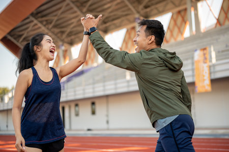Cheerful Asian female and male friends give each other a high five to celebrate their success after running together at a stadium. people, friendship, sportの写真素材