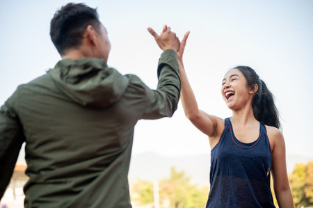 Cheerful Asian female and male friends give each other a high five to celebrate their success after running together at a stadium. people, friendship, sportの写真素材