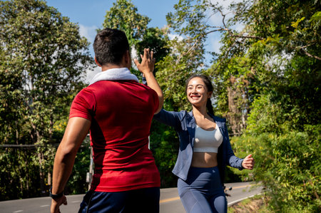 Two cheerful Asian friends give each other a high five to celebrate while running together on a hot, sunny day. people, friendship, sportの写真素材