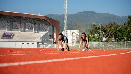 Two determined Asian athlete runners are on the track, getting ready to race in a stadium on a sunny day. competition, challenging, sport game, exercising, trainingの写真素材