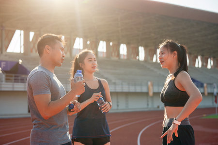 A group of Asian athlete runners enjoy a conversation while resting on a running track after training at a stadium on a bright, sunny day. people and sport conceptsの写真素材