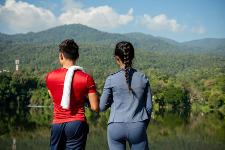 A back view of an Asian man and woman in sportswear, jogging together and admiring the nature view in a park on a summer morning. people and wellbeing lifestyleの写真素材