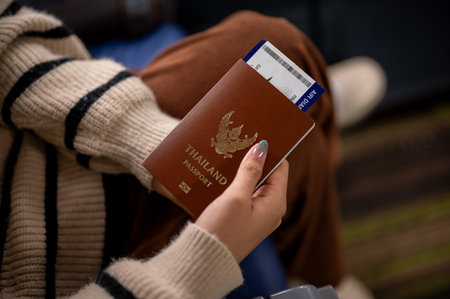 A close-up image of a woman in a cozy knitted sweater holding her Thailand passport and a boarding pass, sitting in the airplane during the flight, traveling to somewhere on her vacation.の写真素材