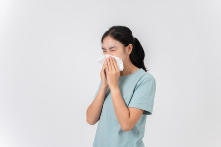 A sick, uncomfortable young Asian woman sneezing and blowing her nose, suffering from a runny nose, flu, allergy, and cold. health care conceptの写真素材