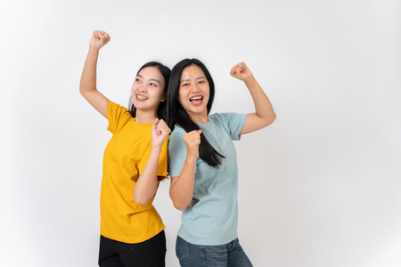 Two joyful, smiling Asian female friends in casual clothes enjoying dancing together against an isolated white studio background. friendship conceptの写真素材